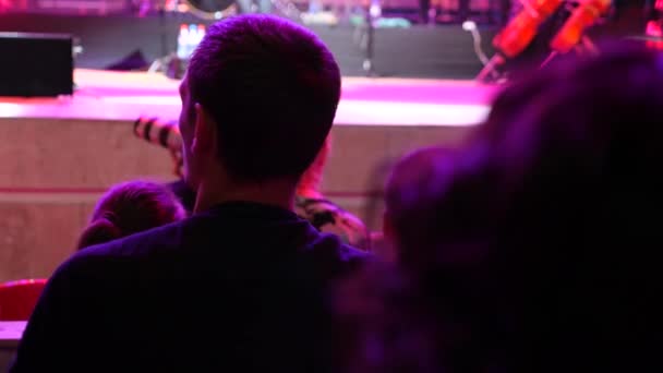 Una multitud de personas iluminadas por la luz colorida durante un concierto de una banda de rock con una orquesta sinfónica. 4k — Vídeo de stock