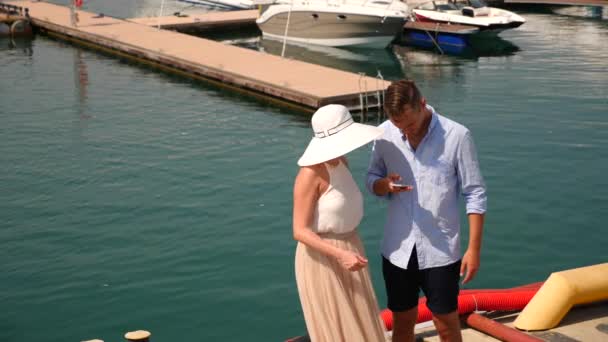 A loving couple is standing on the quay with yachts And looks at the phone. 4K. Slow motion. — Stock Video