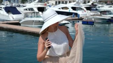 Kadın şapka ve güneş gözlüğü arka planda selfie bay Yatlar ile yapar. Kız bir etek-güneş iplik ve sevindirici. 4 k yavaş hareket.