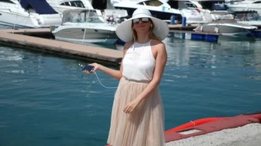 Kadın şapka ve güneş gözlüğü arka planda selfie bay Yatlar ile yapar. Kız bir etek-güneş iplik ve sevindirici. 4 k yavaş hareket.