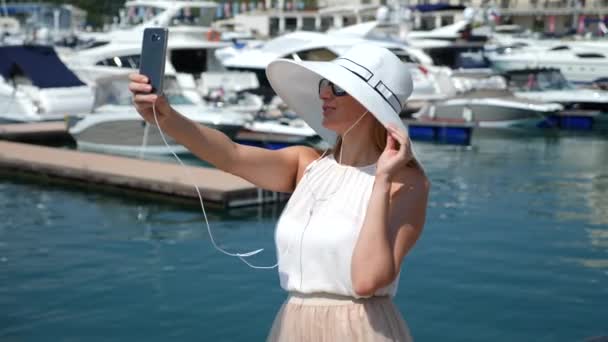 Žena v klobouku a sluneční brýle na pozadí díky selfie bay s jachtami. Dívka v sukni the sun je spinning a radosti. 4 k Zpomalený pohyb. — Stock video