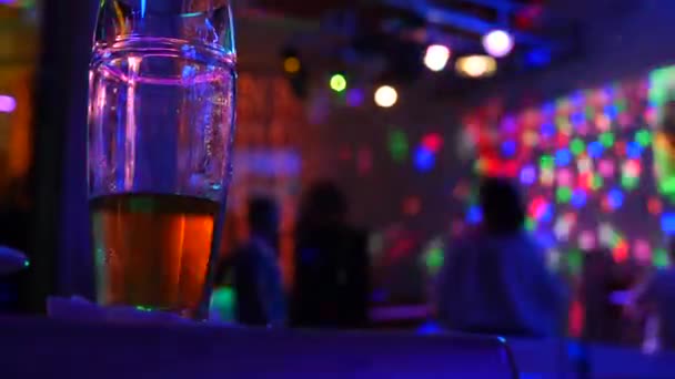 No terminar una taza con cerveza en la mesa en el bar de la discoteca en el fondo de la gente bailando. 4k . — Vídeo de stock