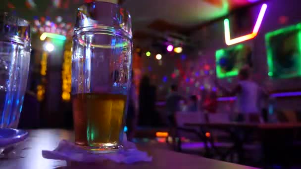 Не допивать кружку с пивом на столе в диско-баре на фоне танцующих людей. 4k . — стоковое видео