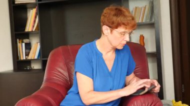 Yaşlı kadın bir deri kanat sandalyede oturan bir mesaj onu Smartphone'da çevirir. 4k, ağır çekim