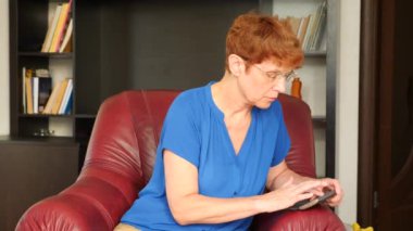 Yaşlı kadın bir deri kanat sandalyede oturan bir mesaj onu Smartphone'da çevirir. 4k, ağır çekim