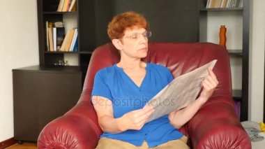 Yaşlı bir deri kanat sandalyede oturan kadın bir gazete okuyor. 4k, ağır çekim