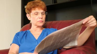 Yaşlı bir deri kanat sandalyede oturan kadın bir gazete okuyor. 4k, ağır çekim