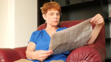 Yaşlı bir deri kanat sandalyede oturan kadın bir gazete okuyor. 4k, ağır çekim