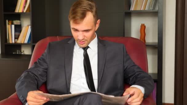 De zakenman is zittend in een stoel en het lezen van een krant. Hij is ongelukkig en expressief. 4. Slow motion. — Stockvideo