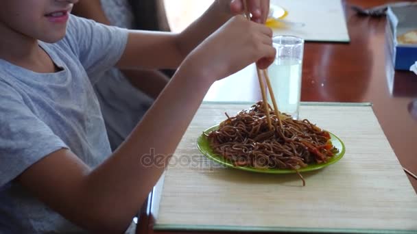 Il ragazzo mangia tagliatelle di grano saraceno con le bacchette. 4k. Tiro al rallentatore . — Video Stock