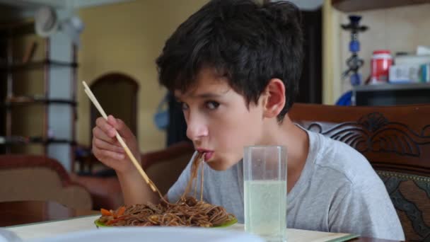 Il ragazzo mangia tagliatelle di grano saraceno con le bacchette. 4k. Tiro al rallentatore . — Video Stock