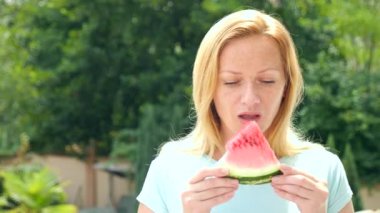 Gökyüzü ve ağaçlar karşı açık havada karpuz yeme genç güzel sarışın bir kadın. 4 k. ağır çekim.