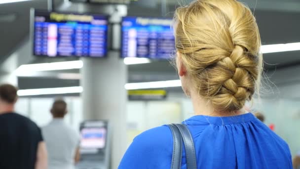 Frau in der Wartehalle des Flughafens. Flugerwartungen am Flughafen. 4k, Zeitlupe, das Mädchen am Flughafen blickt auf die Informationstafel. — Stockvideo