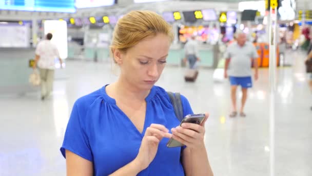 Femeia folosește un smartphone în salonul de așteptare al aeroportului. Aşteptări de zbor la aeroport. 4k, mișcare lentă — Videoclip de stoc