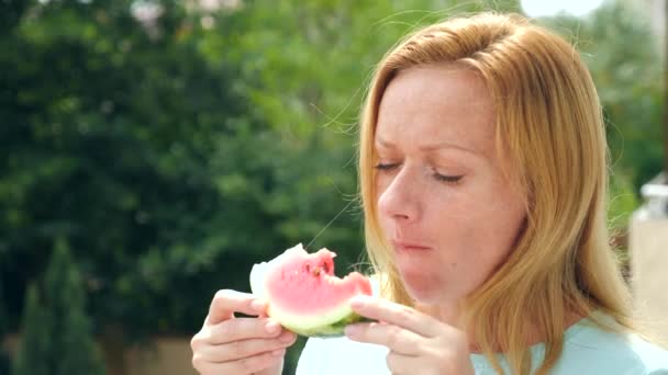 Joven hermosa mujer rubia comiendo sandía al aire libre contra el cielo y los árboles. 4k. Movimiento lento . — Vídeos de Stock