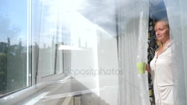 Çekici bir genç kadın ağır çekimde perdeleri açar, onun evinde penceresinin beklemedeyiz gündoğumu, bakar. Bir fincan çay veya kahve. 4 k. ağır çekim.