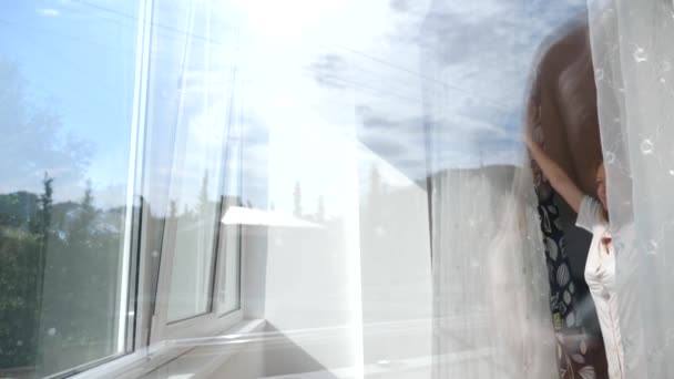 Attraktiv ung kvinna öppnar gardiner i slow motion tittar på sunrise anseende nära fönstret i hennes hem. 4k — Stockvideo