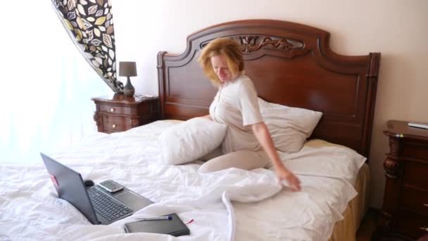 Kobieta w piżamie, tańczy z radości na jej łóżku z radosną wiadomością z jej laptopa. 4k, zwolnionym tempie — Wideo stockowe