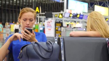 Kadın bir smartphone Havaalanı lounge bekleyen kullanır. Havaalanında uçuş beklentilerini. 4k, ağır çekim