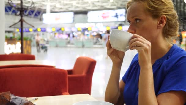 Woman uses a smartphone in airport waiting lounge. She drinks coffee. Expectations of flight at airport. 4k, slow motion — Stock Video