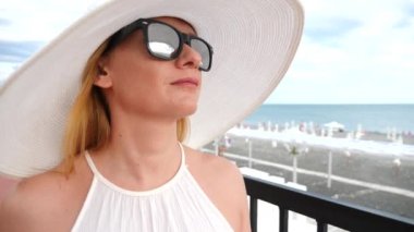 Zarif bir kadın beyaz bir kadın ekledi şapka ve güneş gözlüğü Deniz Manzaralı sahiptir. 4k, ağır çekim