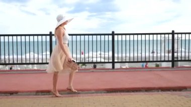 Bir şapka ve beyaz hava elbise zarif bir kadında Rıhtımlar elini kolunu sallaya dönüyor. Genel çekim. 4k, ağır çekim