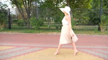Bir şapka ve beyaz hava elbise zarif bir kadında Rıhtımlar elini kolunu sallaya dönüyor. Genel çekim. 4k, ağır çekim