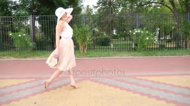 Bir şapka ve beyaz hava elbise zarif bir kadında Rıhtımlar elini kolunu sallaya dönüyor. Genel çekim. 4k, ağır çekim