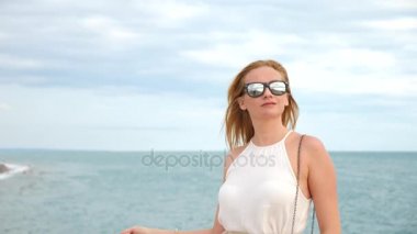 Zarif bir kadın beyaz bir kadın ekledi şapka ve güneş gözlüğü Deniz Manzaralı sahiptir. 4k, ağır çekim