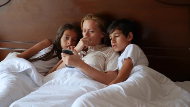 Une famille heureuse regarde quelque chose sur son smartphone alors qu'elle est couchée au lit. 4k, au ralenti . — Video