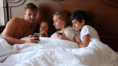 Mutlu bir aile bir şey yatakta yatan süre onların smartphone üzerinde arıyor. 4k, ağır çekim.