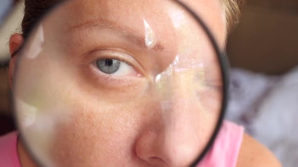 De vrouw zonder make-up met een vergrootglas in een hand. 4k, slow-motion — Stockvideo