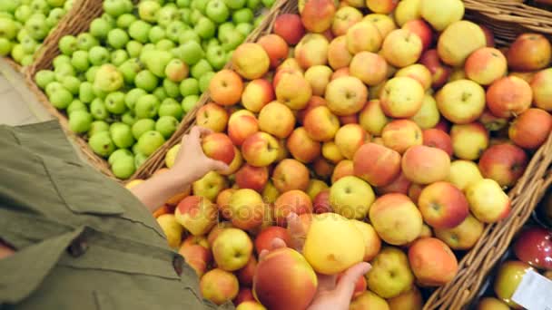 Een vrouw in een supermarkt op een plantaardige plank, koopt groenten en fruit. Man kiest appels. Slowmotion, 4k — Stockvideo