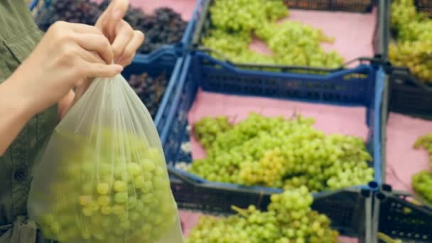 Uma mulher em um supermercado em uma prateleira de vegetais, compra legumes e frutas. O homem escolhe uvas verdes. Movimento lento, 4k — Vídeo de Stock