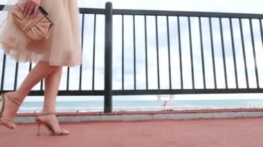 Bir şapka ve beyaz hava elbise zarif bir kadında Rıhtımlar elini kolunu sallaya dönüyor. Bacaklar yakın çekim. 4k, ağır çekim