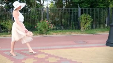 Bir şapka ve beyaz hava elbise zarif bir kadında Rıhtımlar elini kolunu sallaya dönüyor. Genel çekim. 4k, ağır çekim