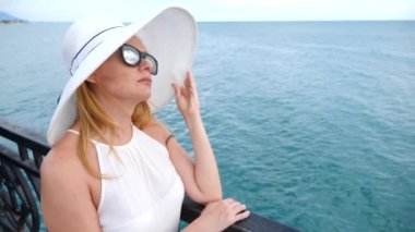 Zarif bir kadın beyaz bir kadın ekledi şapka ve güneş gözlüğü Deniz Manzaralı sahiptir. 4k, ağır çekim