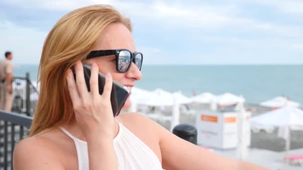 Elegant woman blonde in sunglasses talking on the phone against the sky and tree foliage. view from below. 4k, slow-motion — Stock Video