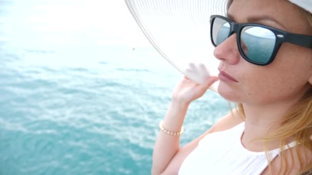 Zarif bir kadın beyaz bir kadın ekledi şapka ve güneş gözlüğü Deniz Manzaralı sahiptir. 4k, ağır çekim — Stok video