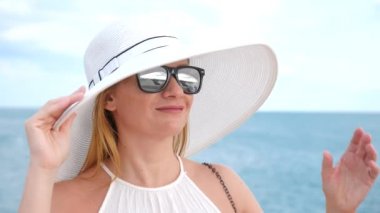 Zarif bir kadın beyaz bir kadın ekledi şapka ve güneş gözlüğü Deniz Manzaralı sahiptir. 4k, ağır çekim