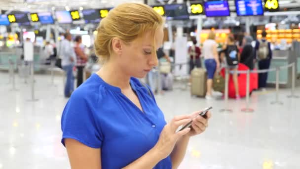 Kvinnan använder en smartphone i flygplats väntar lounge. Förväntningar på flyg på flygplatsen. 4k, Slowmotion — Stockvideo