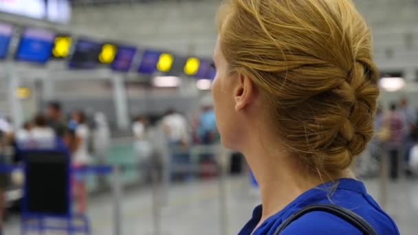 Frau in der Wartehalle des Flughafens. Flugerwartungen am Flughafen. 4k, Zeitlupe, das Mädchen am Flughafen blickt auf die Informationstafel. — Stockvideo