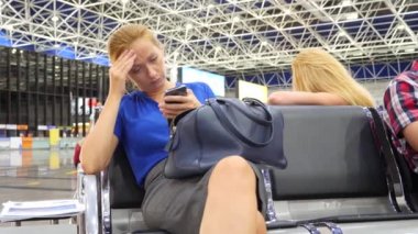 Kadın bir smartphone Havaalanı lounge bekleyen kullanır. Havaalanında uçuş beklentilerini. 4k, ağır çekim