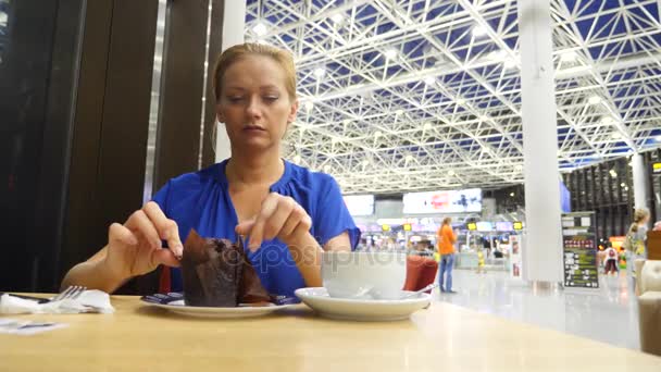 Mulher usa um smartphone na sala de espera do aeroporto. Ela bebe café. Expectativas de voo no aeroporto. 4k, câmera lenta — Vídeo de Stock