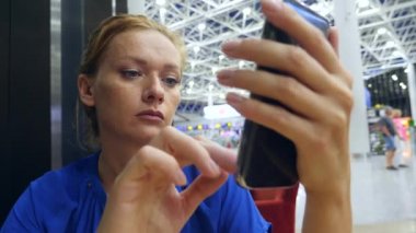 Kadın bir smartphone Havaalanı lounge bekleyen kullanır. Havaalanında uçuş beklentilerini. 4k, ağır çekim