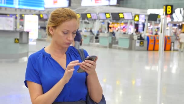 Mujer utiliza un teléfono inteligente en la sala de espera del aeropuerto. Expectativas de vuelo en el aeropuerto. 4k, cámara lenta — Vídeos de Stock