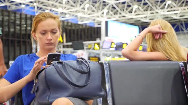 Mulher usa um smartphone na sala de espera do aeroporto. Expectativas de voo no aeroporto. 4k, câmera lenta — Vídeo de Stock