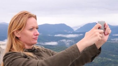 Yavaş çekimde bir selfie alarak dağın tepesine genç kadın. Genç uzun yürüyüşe çıkan kimse kadın alarak dağın zirvesine dağlardan telefonunuza bir görünümünü fotoğraflar. 4k