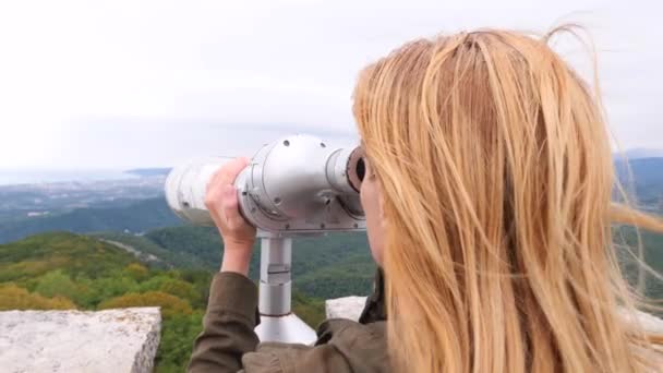 Donna viaggiatore biondo guardando attraverso un telescopio sulla cima di una montagna. 4k, rallentatore — Video Stock