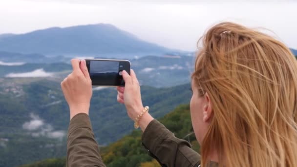Mujer joven en la cima de la montaña tomando una selfie en cámara lenta. Joven excursionista tomando fotografías de una vista de las montañas desde la cima de la montaña hasta su teléfono. 4k — Vídeos de Stock